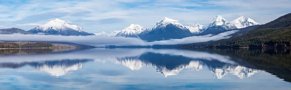 Fog over Lake McDonald beneath forested mountains