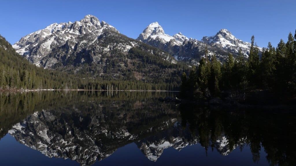 Taggart Lake with Teton Range reflected in still water at the end of the trail