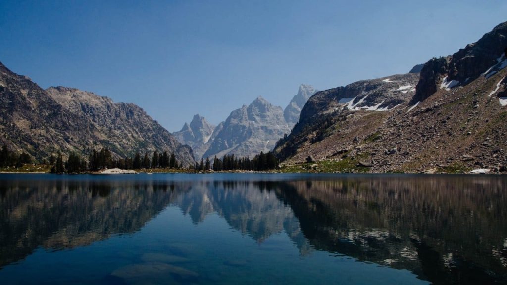 Lake Solitude alpine lake surrounded by Teton peaks on three sides with snow patches