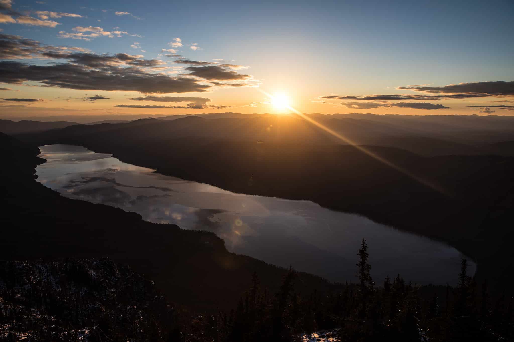 Sunrise over Lake McDonald in Glacier National Park, golden light reflecting off calm water with colorful pebbles visible along the shoreline