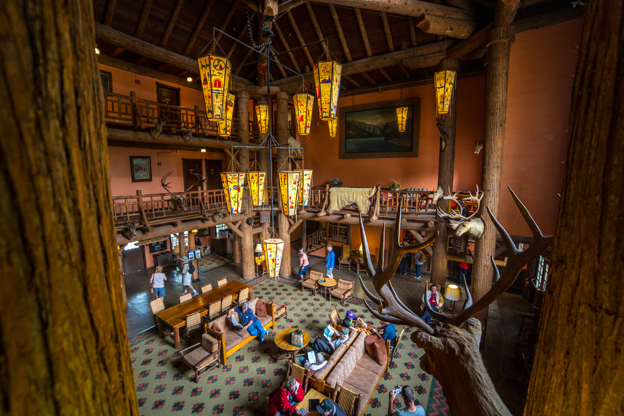 Inside the Many Glacier Hotel lobby in Glacier National Park, rustic logs and warm lanterns set a cozy, grand interior.