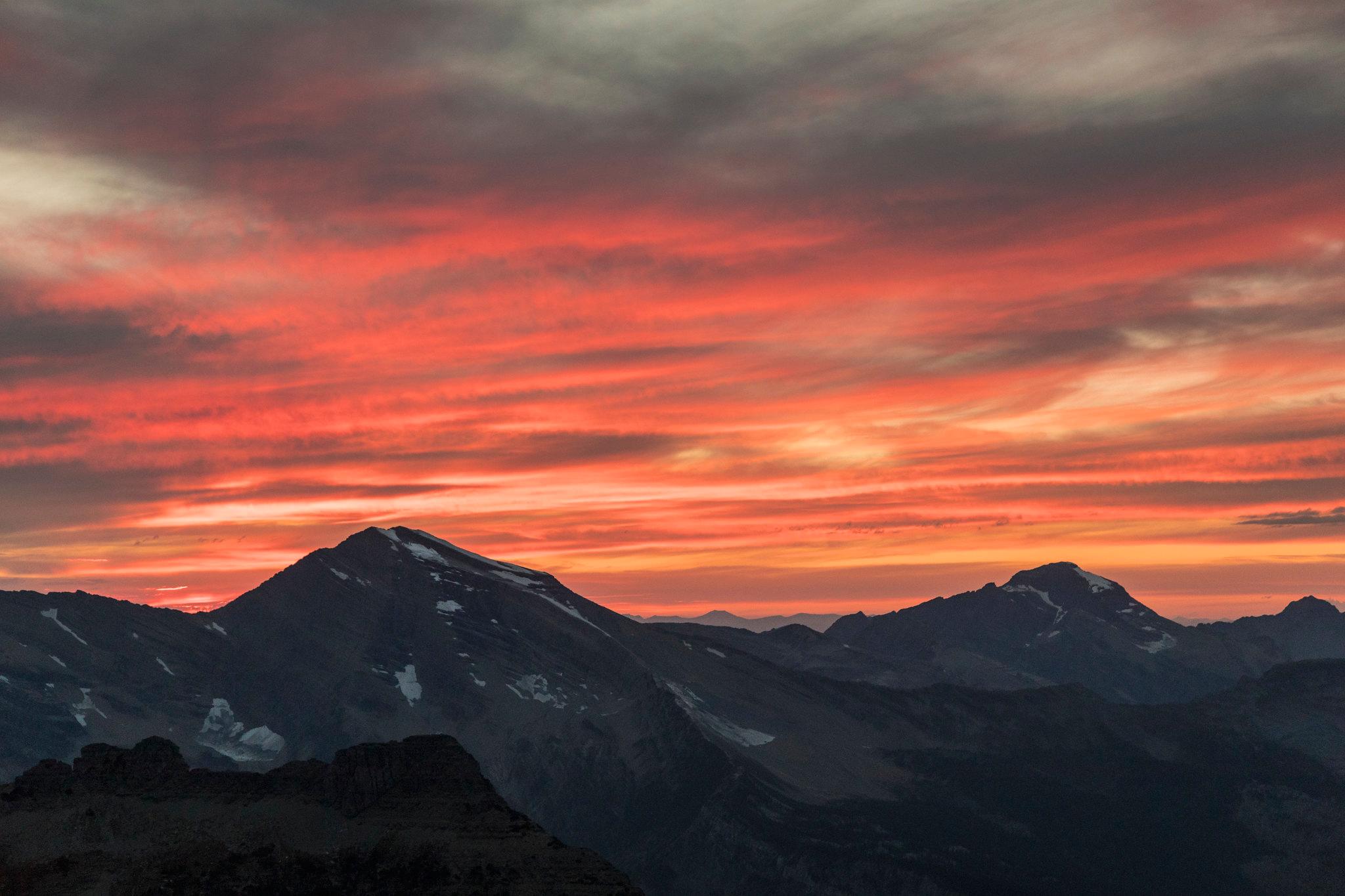 Sunset over jagged Glacier National Park peaks with snow patches along the ridges.