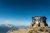 Small stone-lookout cabin perched on a rocky summit in Glacier National Park under a clear blue sky.
