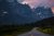 Jagged peaks rise out of a forested valley and an empty road curves off into the distance.