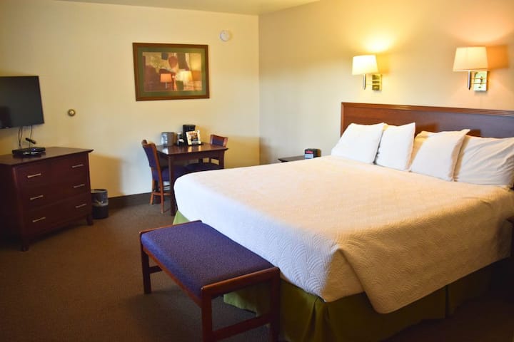 Guest room interior at a lodge-style lodging in Glacier National Park, featuring a large bed, bench, and warm lighting.