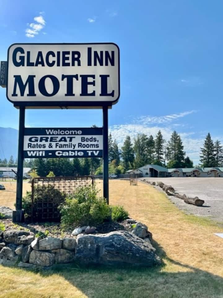 Motel sign at a lodging along a park road in Glacier National Park, with a gravel lot and evergreen trees nearby.