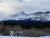 Summit Mountain rises above snow-covered Glacier National Park, with forested slopes and a pale winter sky.