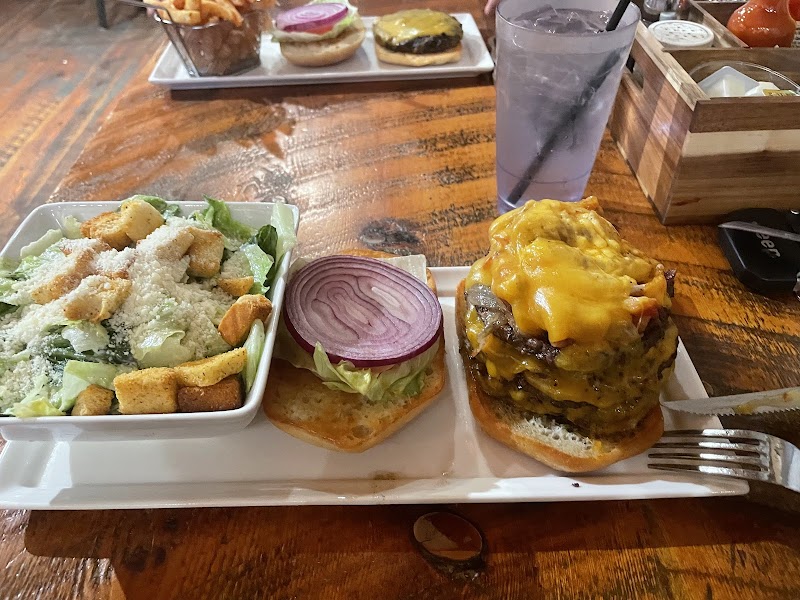 Plate with wedge salad, onion slice on bun, and a tall cheeseburger on a rustic wooden table in Yellowstone National Park.