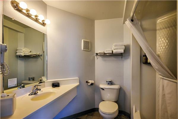 Bright bathroom with white vanity, single sink, mirror, towel shelves, toilet, and a shower with a curtain in Yellowstone.