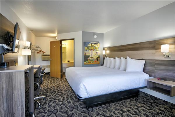 Spacious hotel room with a king bed, linens, wood headboard, desk, and a flat-screen TV in Yellowstone National Park.