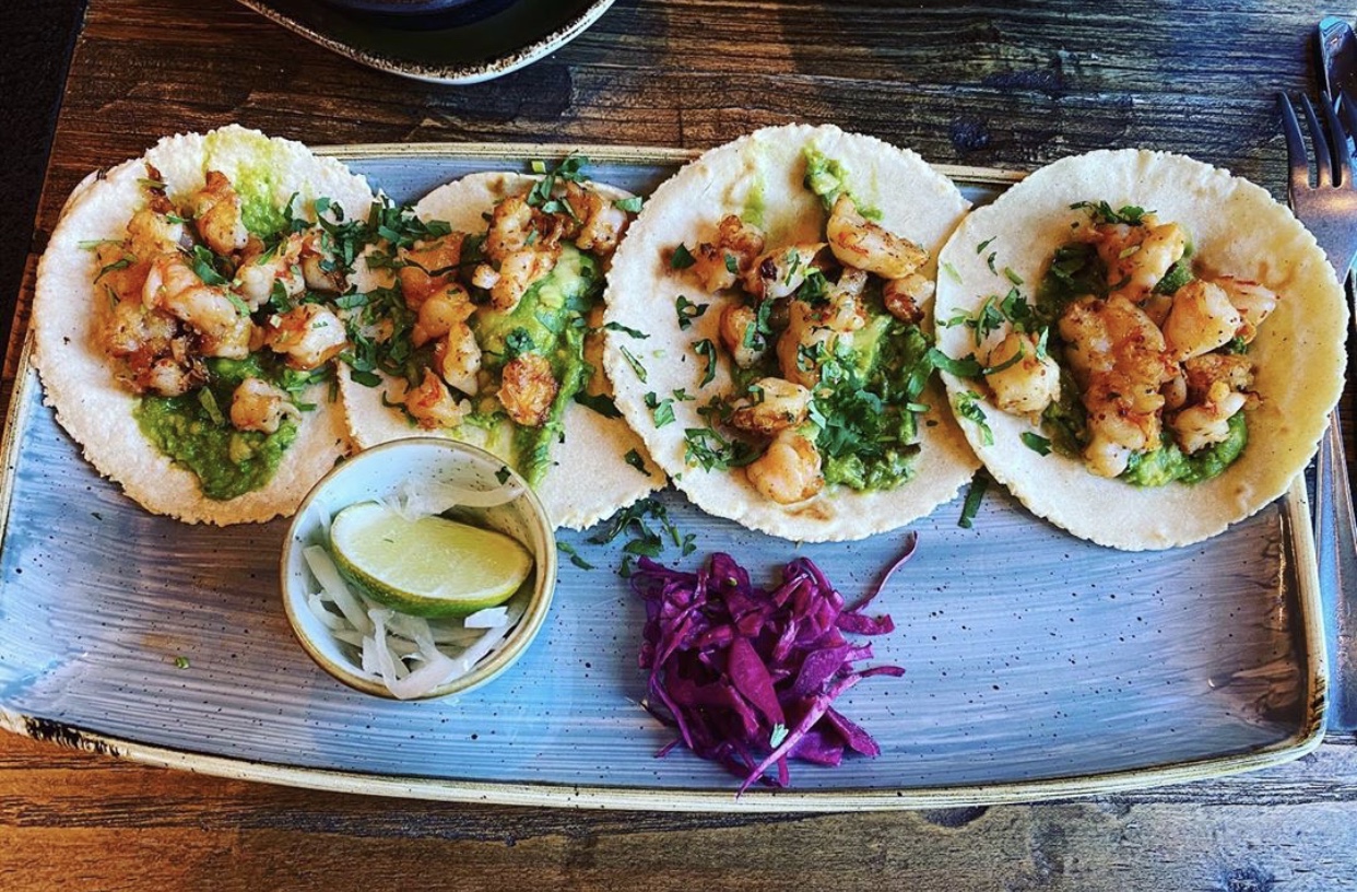 Three shrimp tacos topped with cilantro on a rustic plate with lime and onions, served in Glacier National Park.