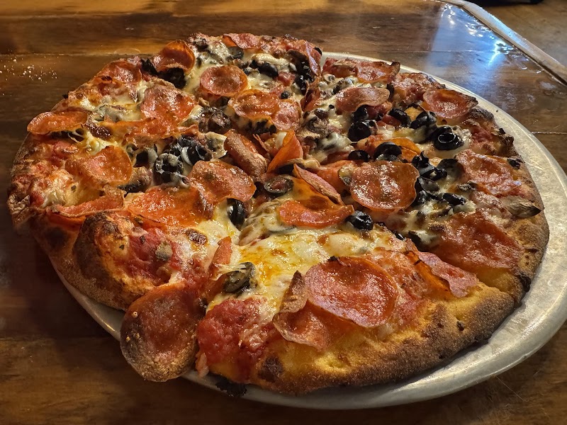 Large pepperoni pizza with black olives and sausage on a golden crust, served on a round metal tray in Yellowstone National Park.