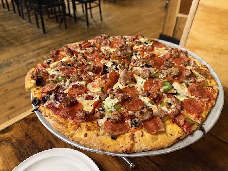 Loaded pepperoni, sausage, olives, peppers, and onions pizza on a metal tray in a Yellowstone National Park dining room.