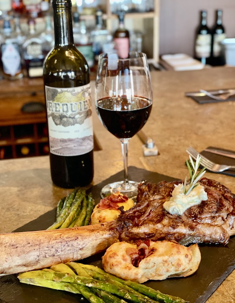 A plated ribeye steak with herb butter, roasted potatoes, and asparagus, plus a glass of red wine in Yellowstone National Park dining venue.