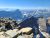 Craggy rocky ledges overlook a snow-dusted canyon and jagged peaks in Glacier National Park under a clear blue sky.