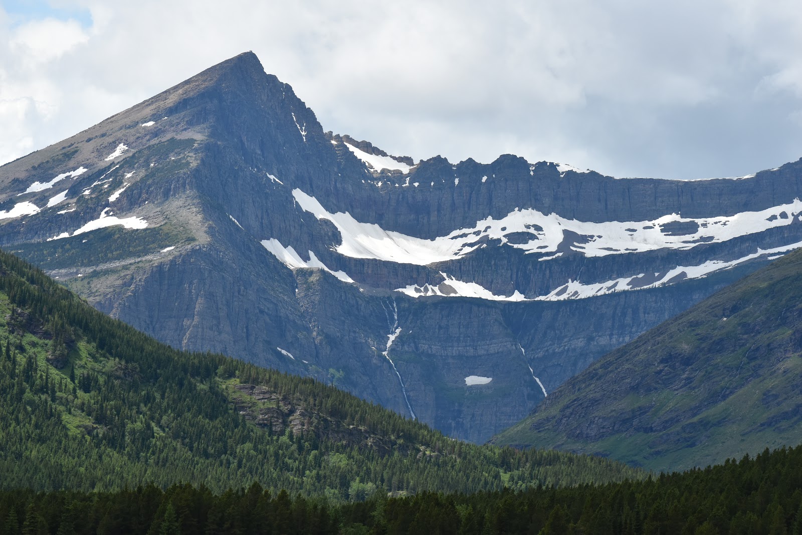 Snow-dusted jagged peaks rise above evergreen forests as Mount Siyeh towers over the glacier-carved valley in Glacier National Park.