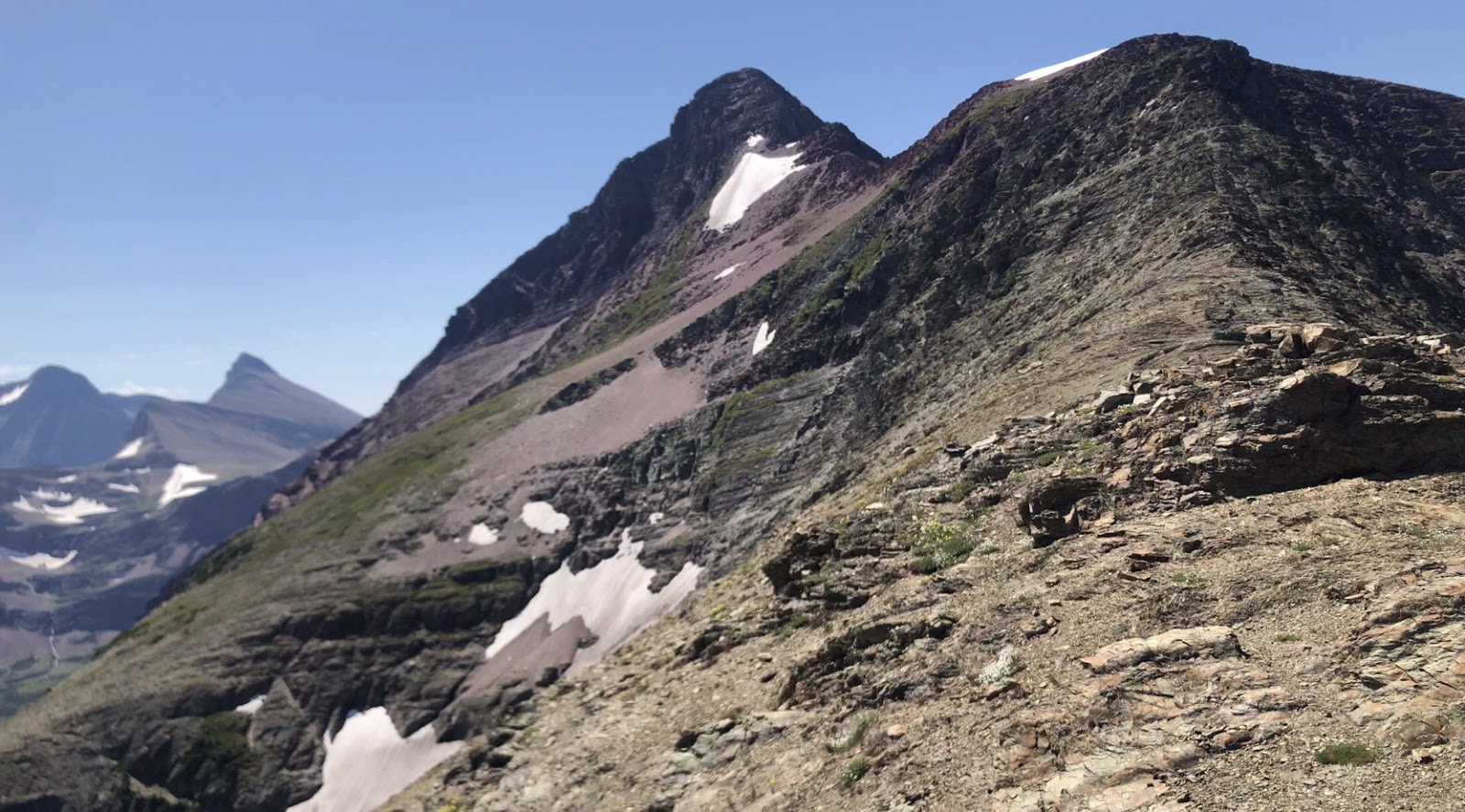 Rugged, rocky Mount Siyeh ridge in Glacier National Park with sparse snow patches under a clear blue sky.