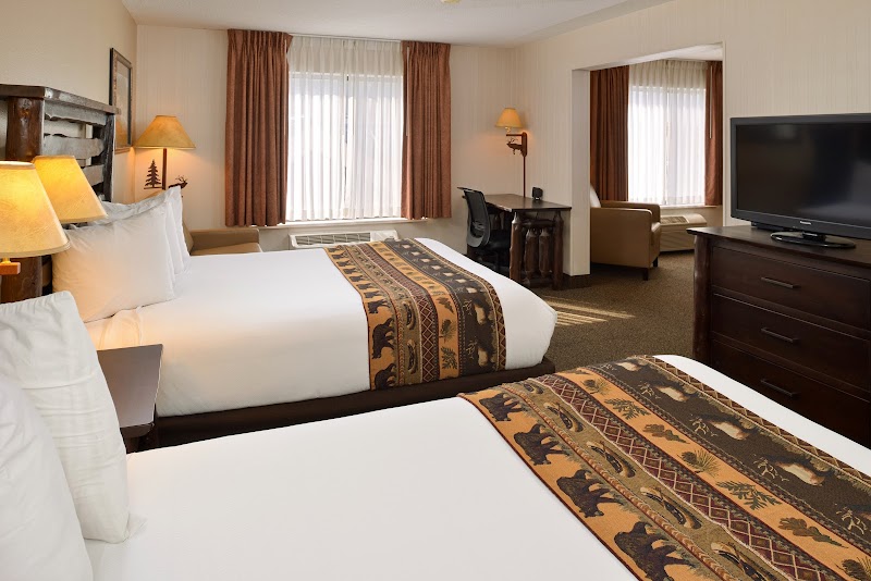 Two queen beds with bear-patterned runners and wood headboards, lamps, a desk, and a TV in a Yellowstone National Park room.