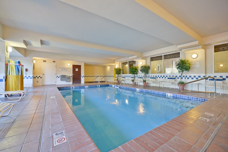 Indoor hotel pool area with blue water, brick-tiled deck, white lounge chairs, and potted plants at Yellowstone National Park.