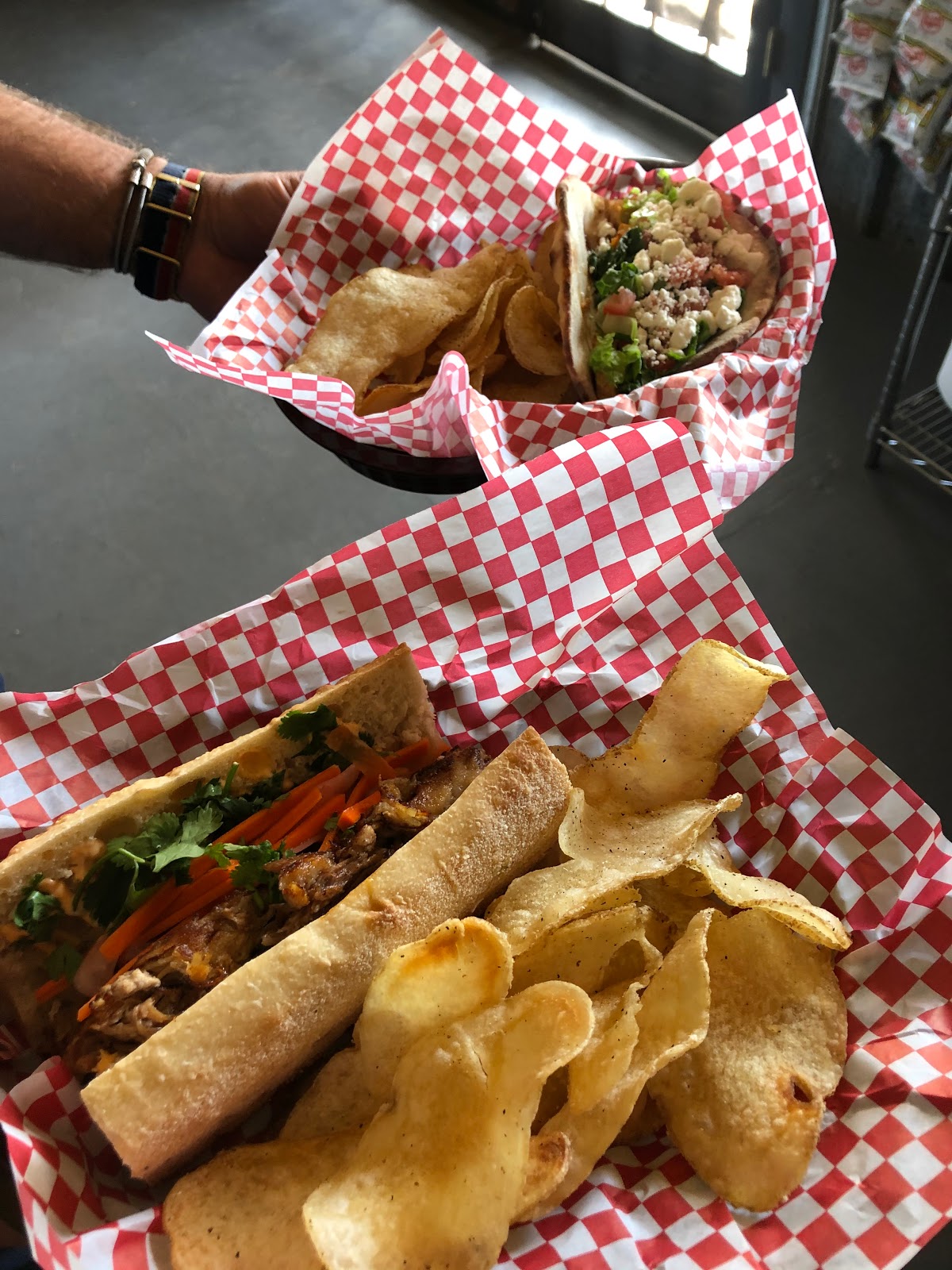 Sandwich with shredded meat and vegetables, a taco, and crisp tortilla chips on red-checkered paper, Glacier National Park.