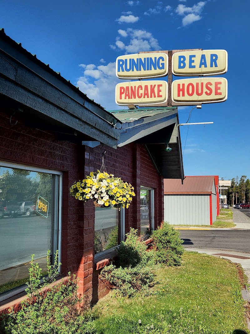 Yellowstone National Park storefront with brick walls, a hanging yellow flower basket, and a large retro sign against a blue sky.
