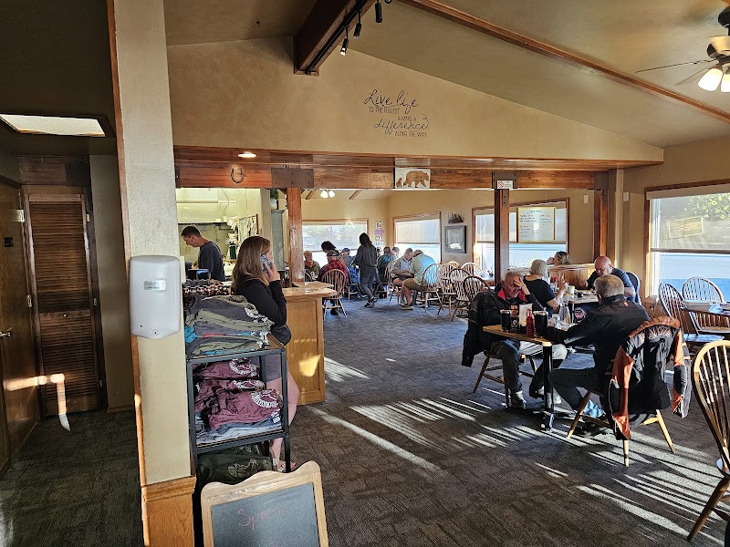 Busy dining room with wooden beams, diners at tables, a server near a counter, sunlight in Yellowstone National Park.