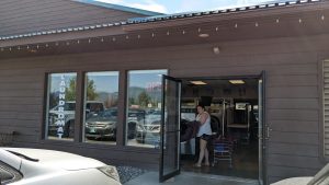 Laundromat storefront with open doors in Glacier National Park, reflections of parked cars in the window.