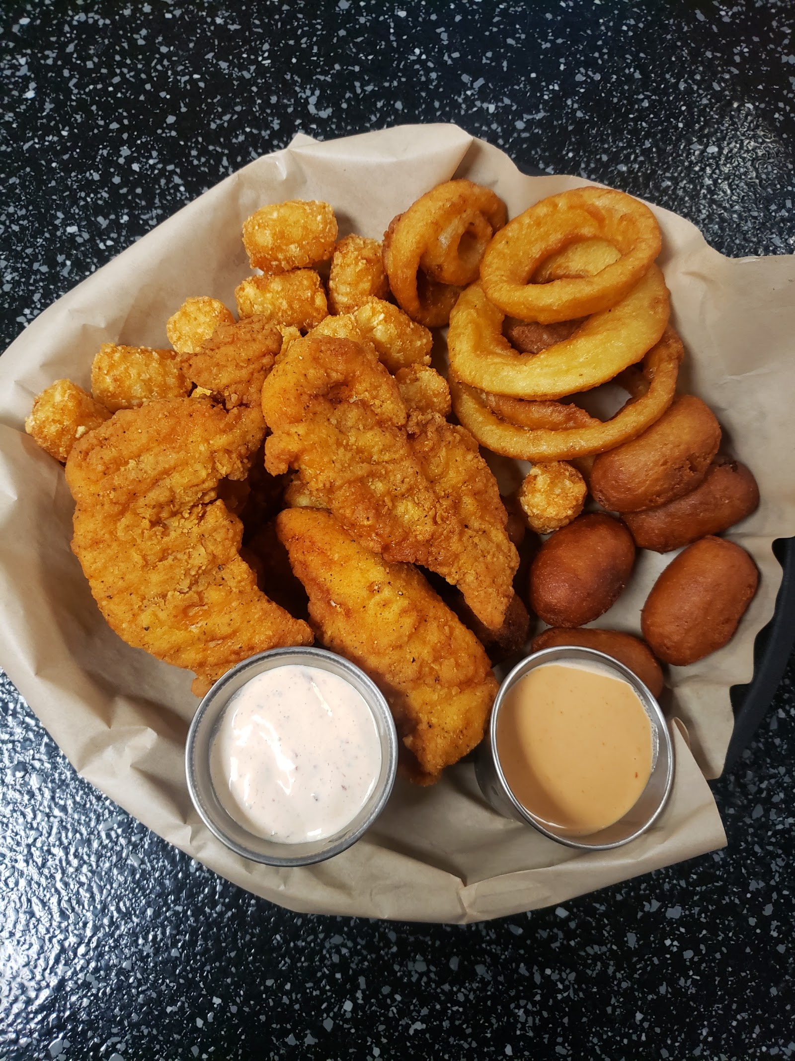 Crispy fried chicken tenders with onion rings and dipping sauces served at a Glacier National Park dining spot.