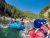 Rafting party navigates whitewater on a glacier-fed river in Glacier National Park, surrounded by forested peaks.