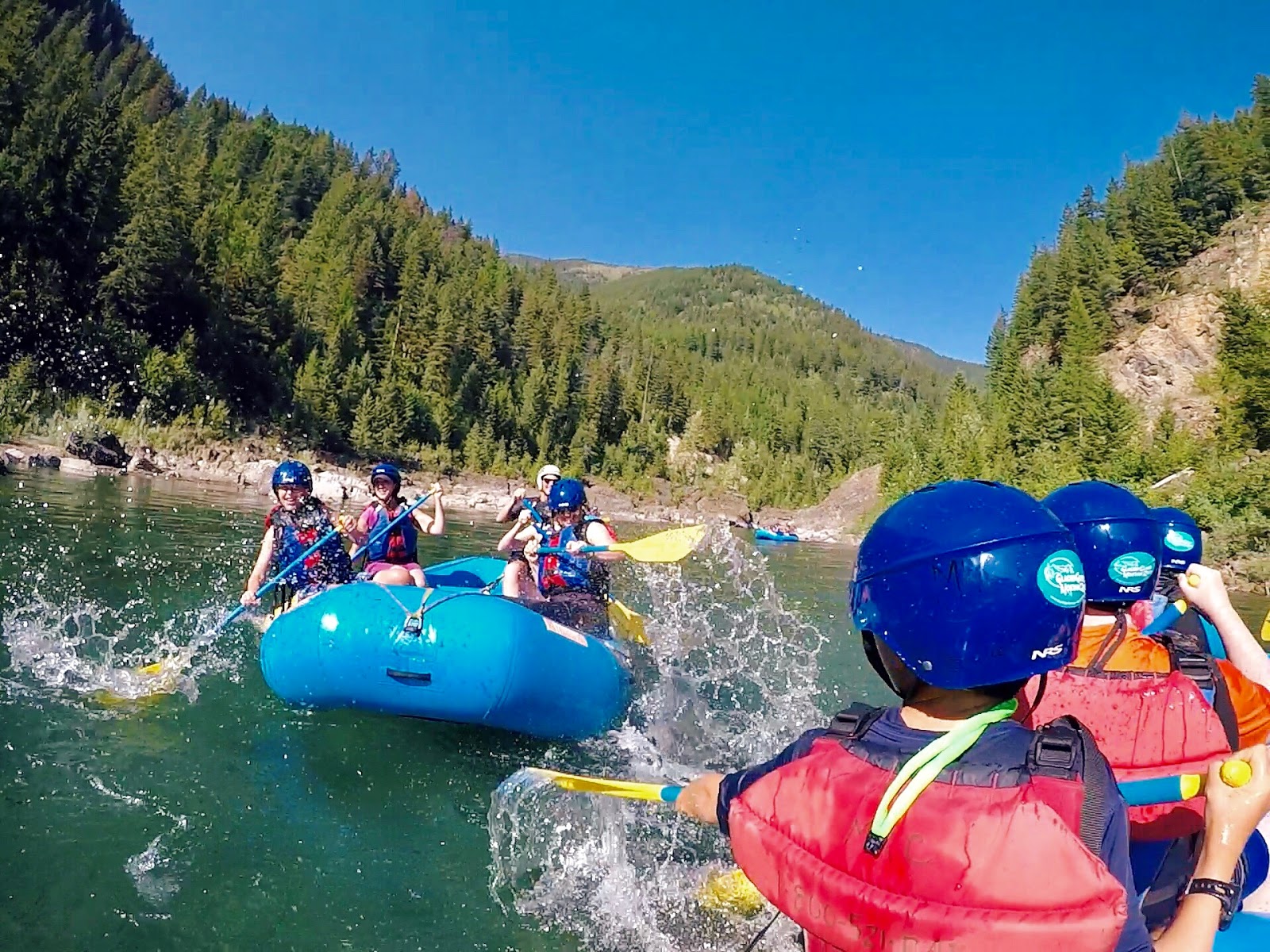 Rafting party navigates whitewater on a glacier-fed river in Glacier National Park, surrounded by forested peaks.