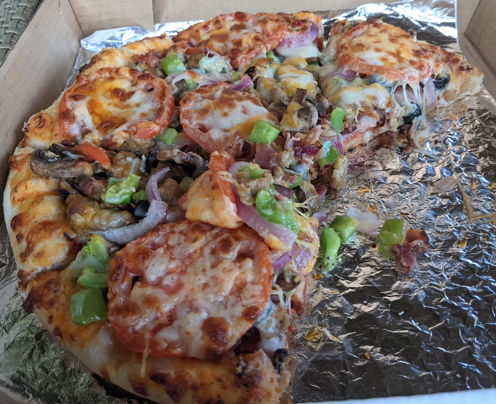 Pizza at a tavern in Glacier National Park, with melted cheese, toppings, and takeaway foil after-bite.
