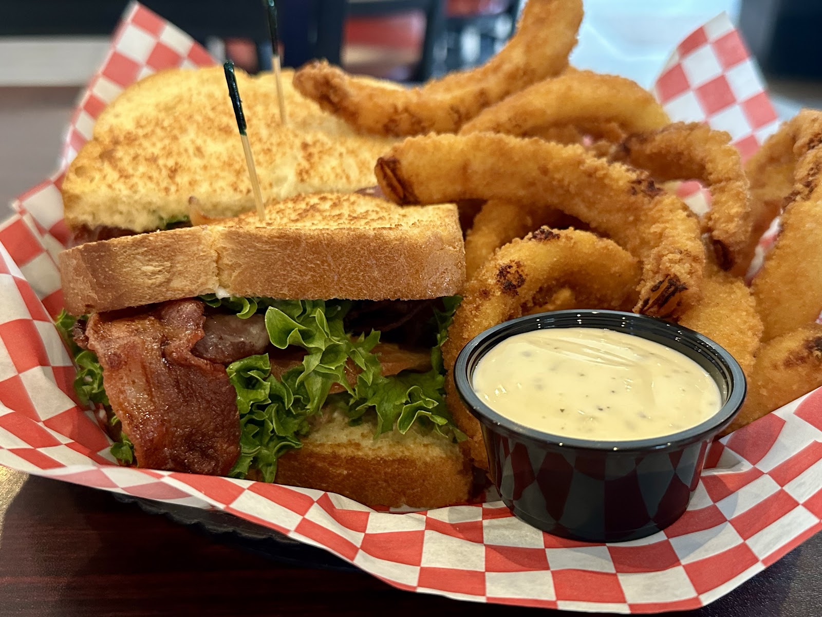 Beef bacon cheeseburger with greens and a side of crispy onion rings at a Glacier National Park dining spot, with a dipping sauce nearby.