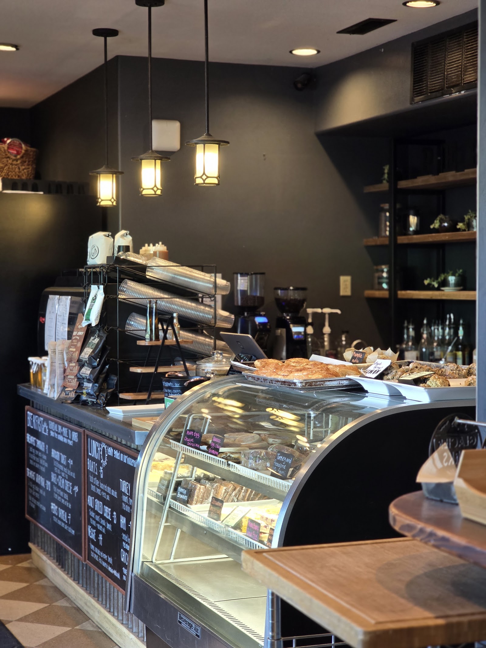 Cozy coffee shop counter and pastry case inside a Glacier National Park cafe, with warm pendant lights and dark walls.