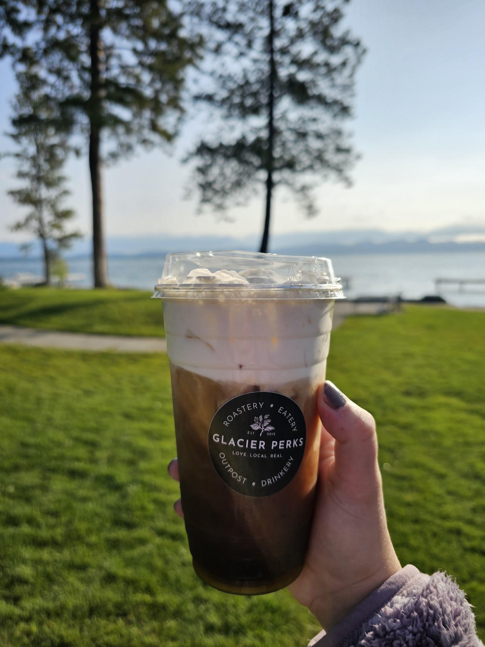 Lake McDonald shore in Glacier National Park with an iced coffee cup in the foreground.