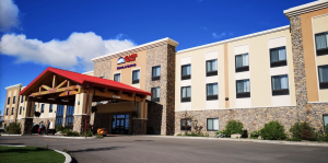 Stone-and-beige hotel with a red porte-cochere, stone accents, and large windows under a bright blue sky at Glacier National Park.