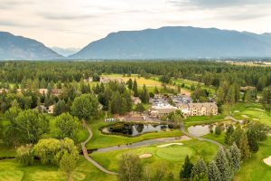 A golf course setting at Glacier National Park with lush greens, ponds, and pine forests visible from above.