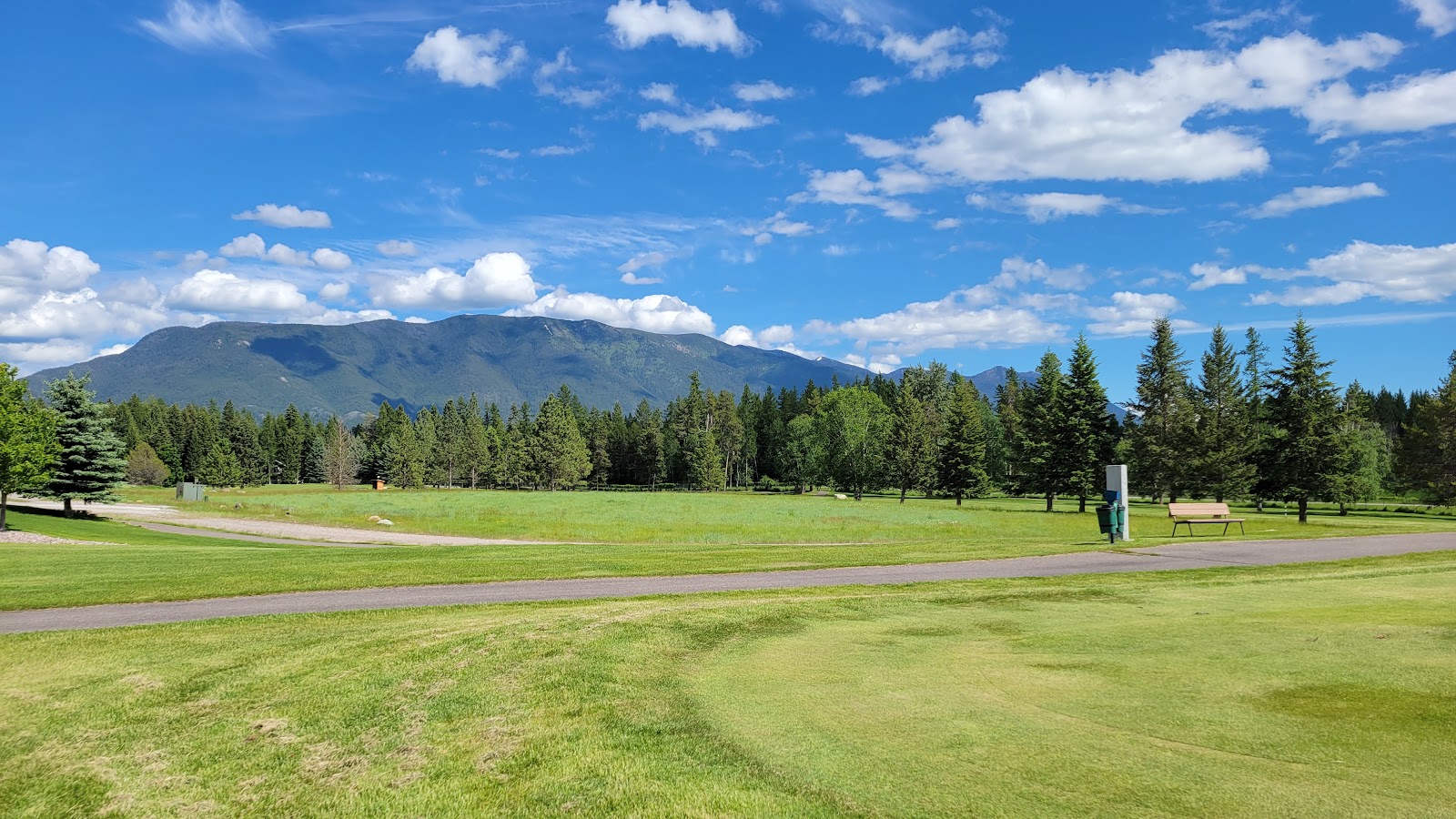 Meadow Lake Golf Course at Glacier National Park showcases emerald fairways, evergreen trees, and distant snow-capped mountains.