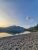 Sunset over a calm lake at Glacier National Park with a pebbled beach, pine shoreline, and distant rugged mountains.