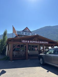 Exterior of a rustic cafe in Glacier National Park with Elk & Buffalo Burgers sign and wooden porch.