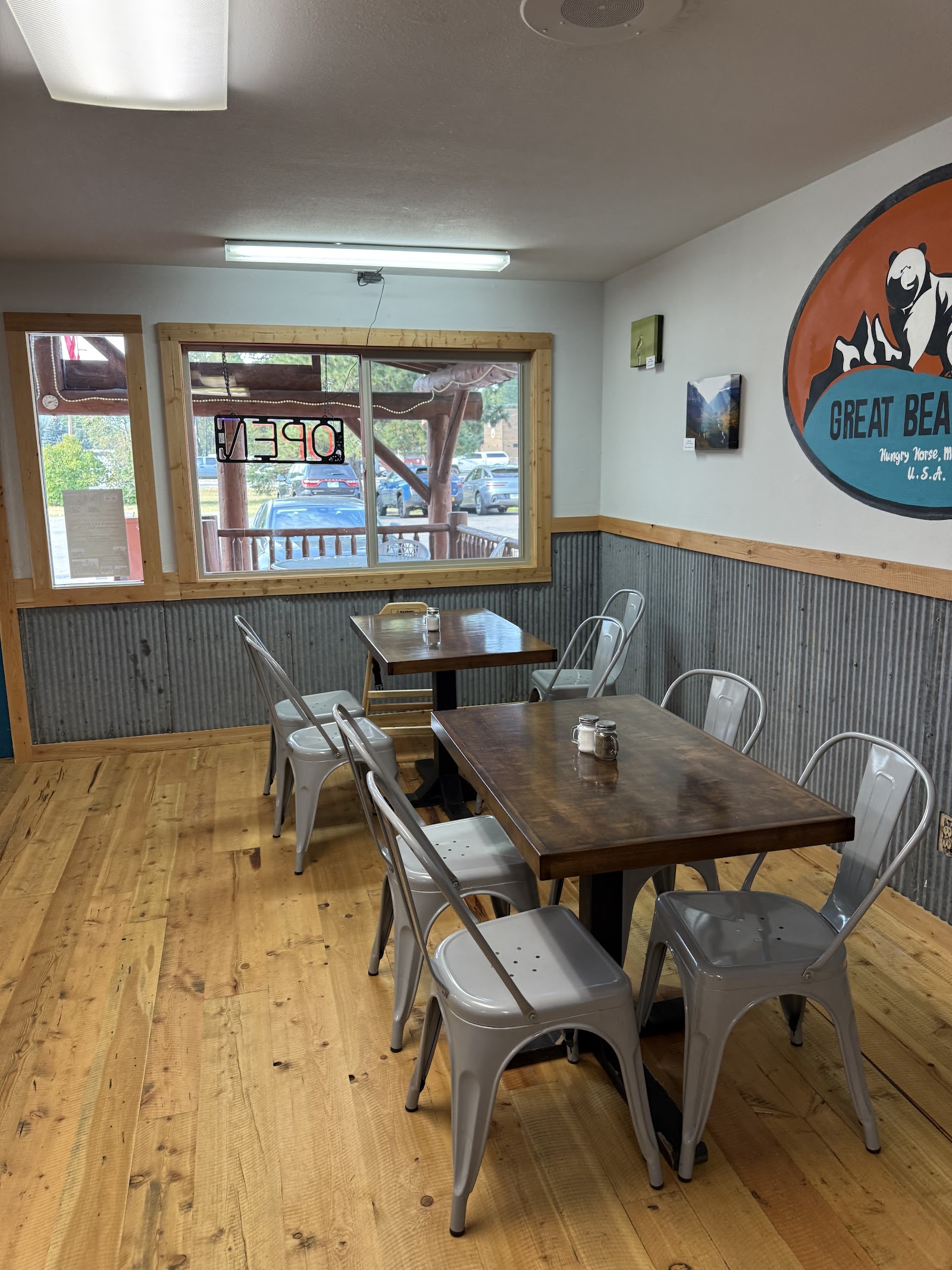 Interior of a rustic cafe in Glacier National Park, with wooden floors, metal chairs, and two-by-two tables.