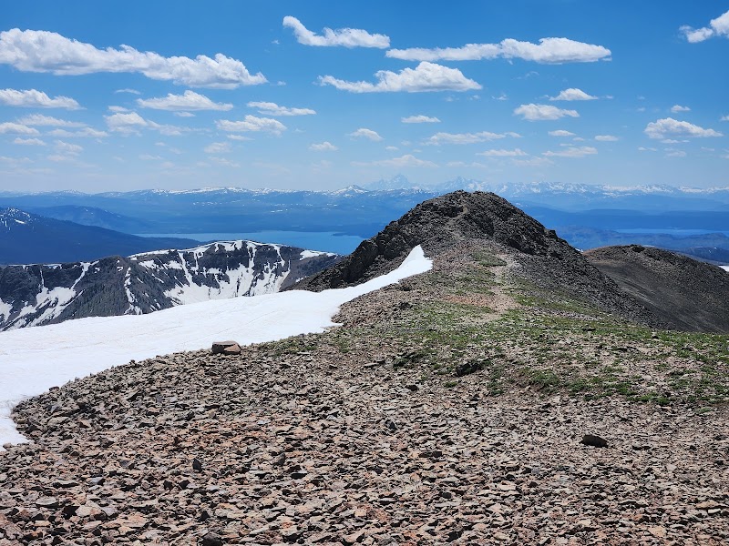 Rugged rocky trail along Avalanche Peak in Yellowstone National Park, with snow patches, distant mountains and blue sky.