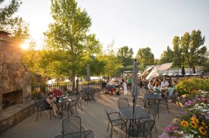 Outdoor restaurant patio near Meadow Lake with dining tables, umbrellas, and a riverbank in Glacier National Park.