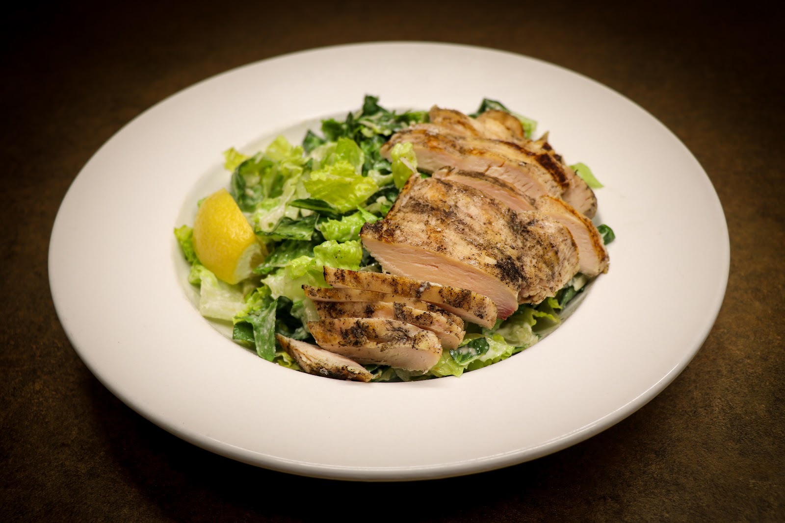 Sliced grilled chicken atop a mixed greens salad with a lemon wedge at a Glacier National Park dining spot.