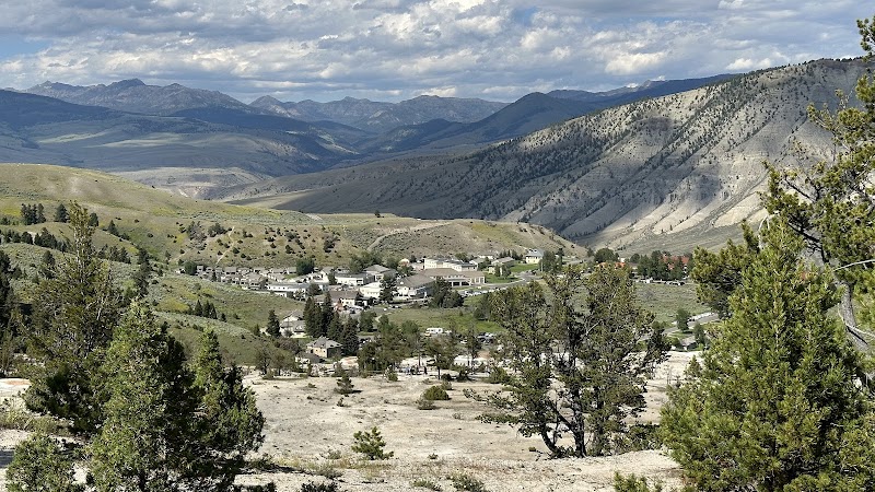 Fort Yellowstone Overlook, Yellowstone National Park, shows a valley village with pines and distant rugged mountains under a cloudy sky.