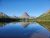 Clear blue lake reflects the jagged mountain peaks and evergreen forest in Glacier National Park.