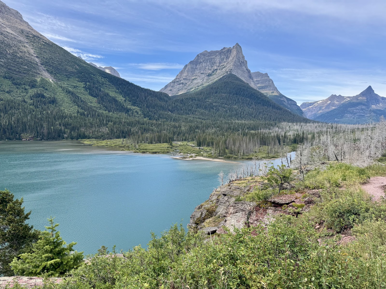 View over Lake McDonald at Glacier National Park, with towering peaks and a forested shoreline under blue skies.