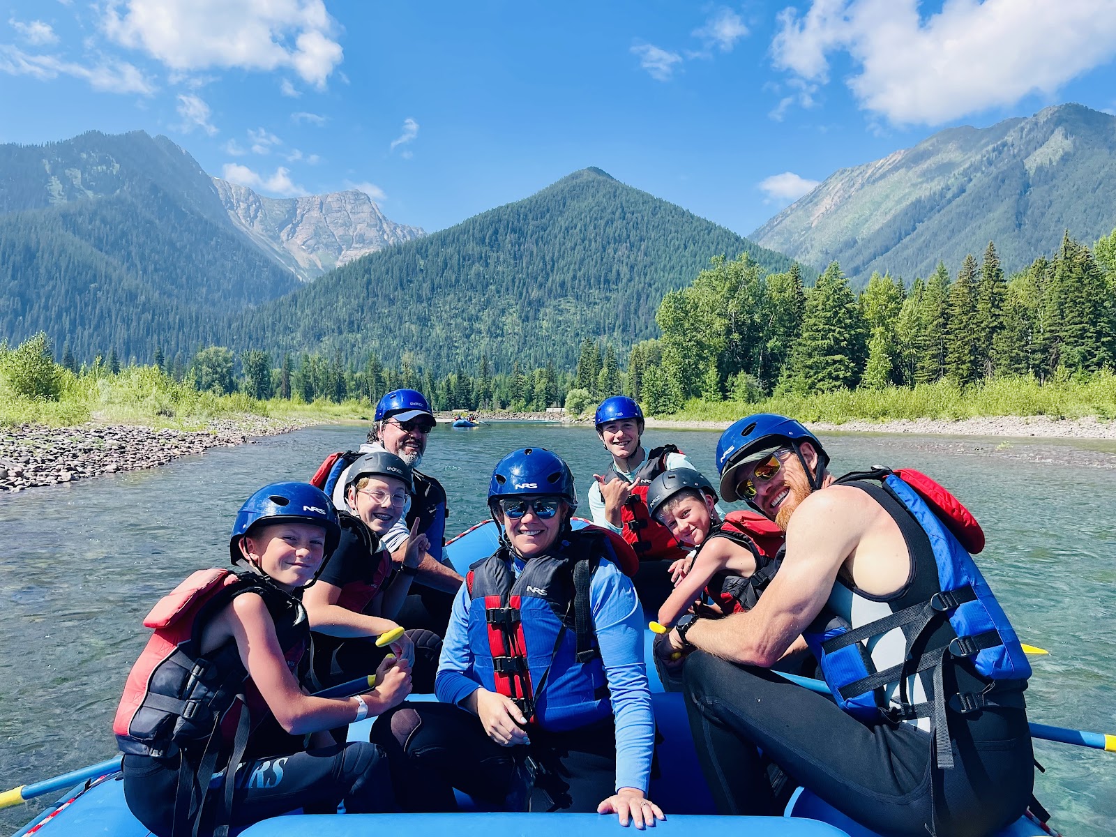 Group of rafters on the Flathead River through Glacier National Park, with forested mountains in view.