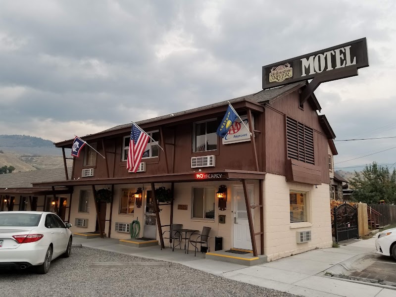 Two-story brown and beige motel with flags, a large MOTEL sign, and cars in a gravel lot at Yellowstone National Park.
