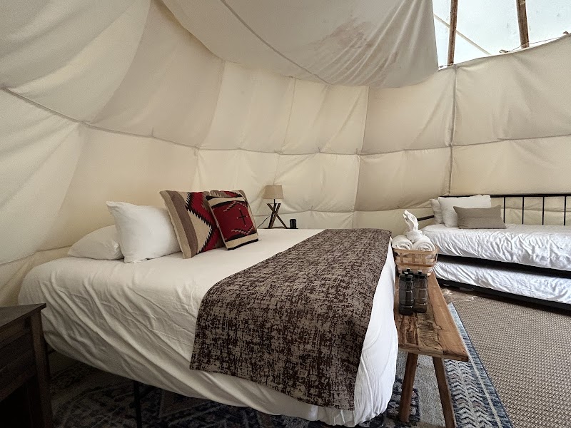 Interior of a white canvas tipi in Yellowstone National Park with two beds, pillows, a brown runner, and a wooden table.