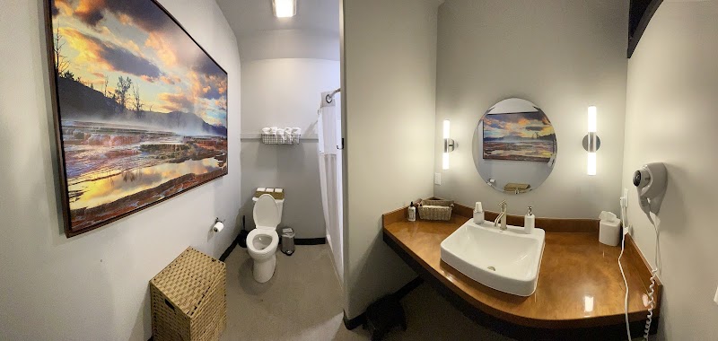 Lodge bathroom in Yellowstone National Park with countertop sink, round mirror, sunset landscape art, toilet, and shower.